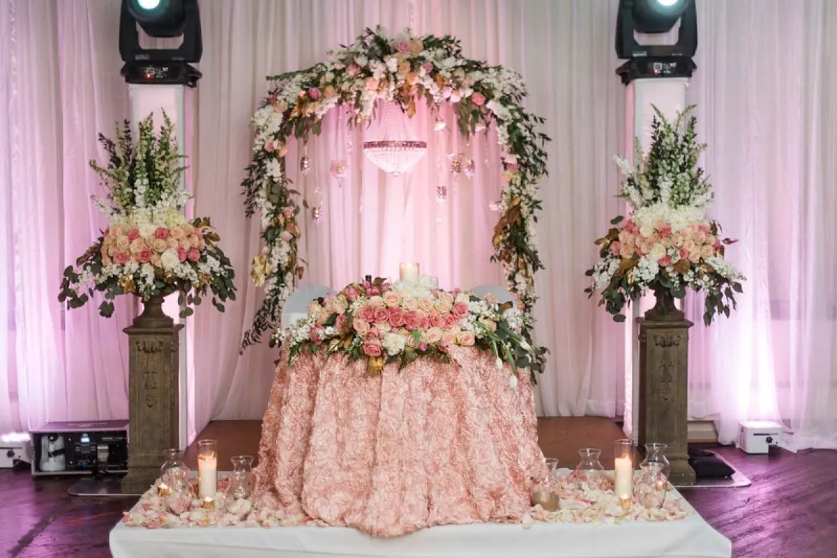 Pink floral arch and sweetheart table lit with uplighting for a wedding reception