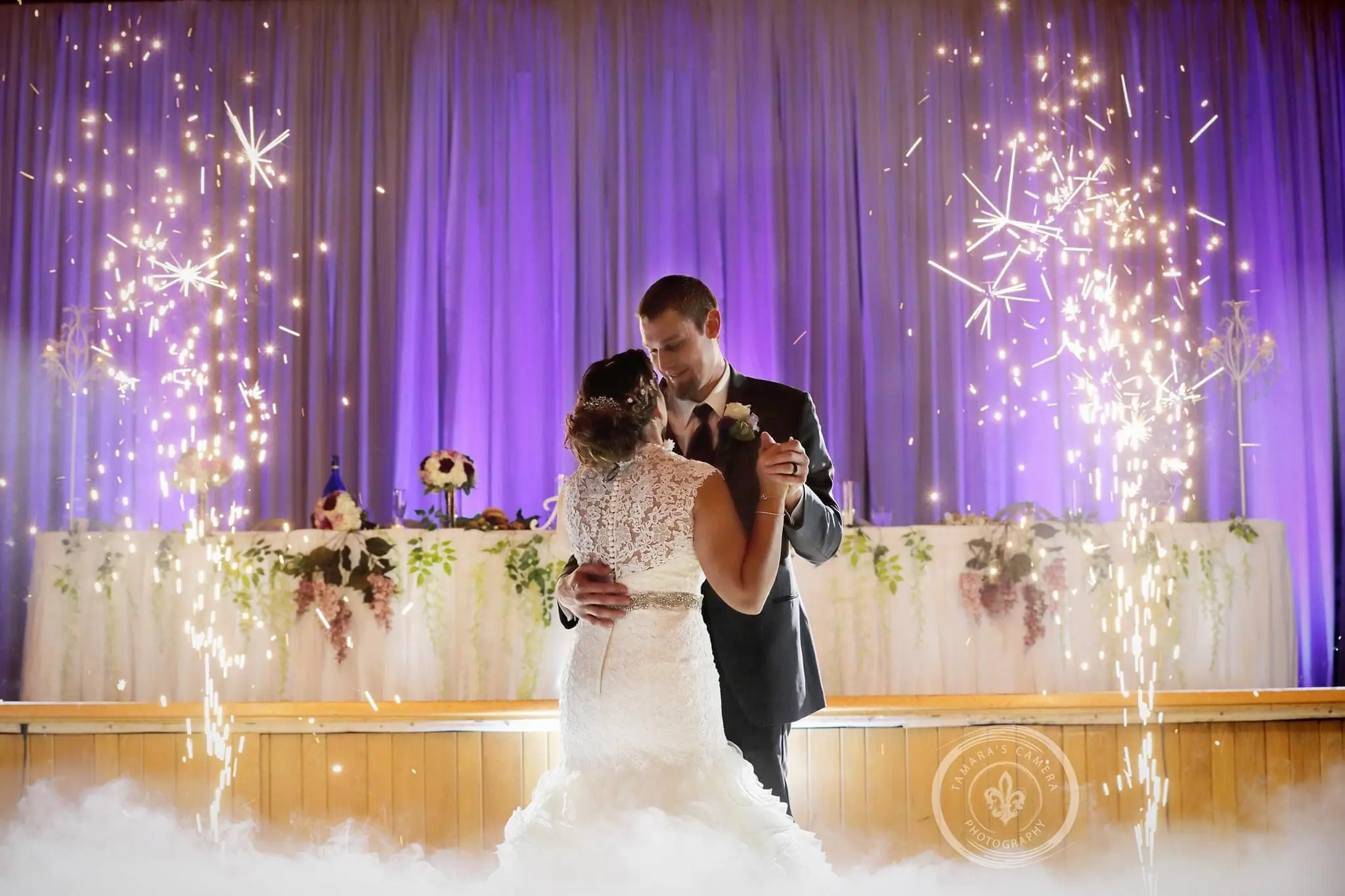 Couple’s first dance with cold sparklers and purple draping lit behind the head table