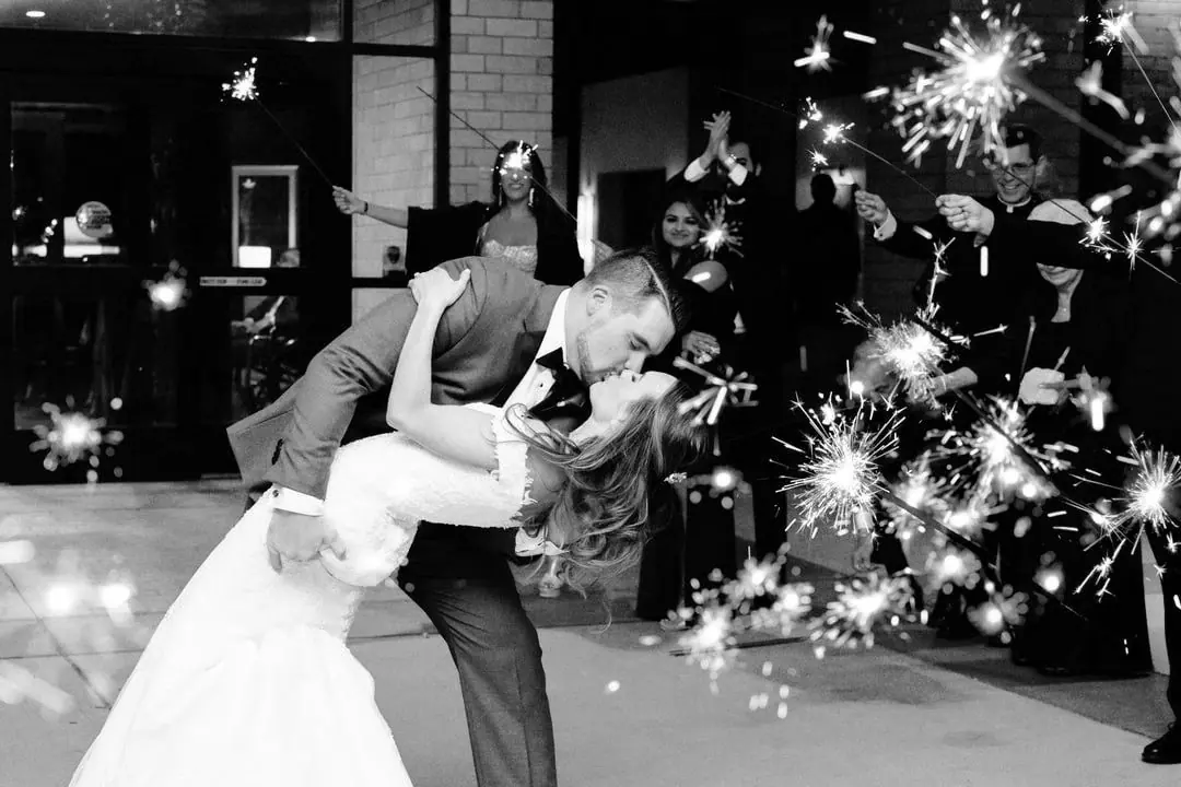 Groom dips and kisses his bride while wedding sparklers burst around them