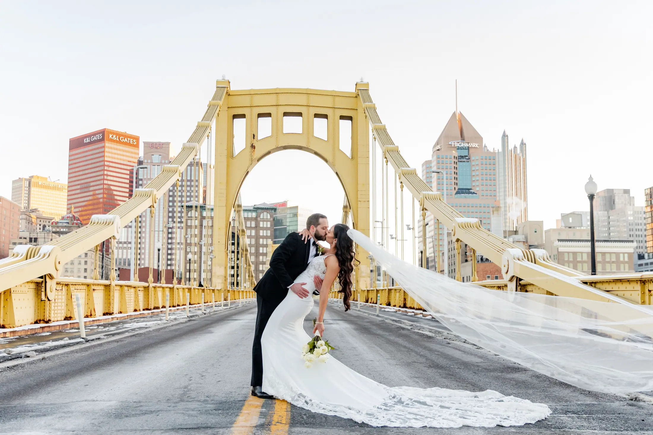 Bride and groom kiss on a Pittsburgh bridge with the city skyline behind them